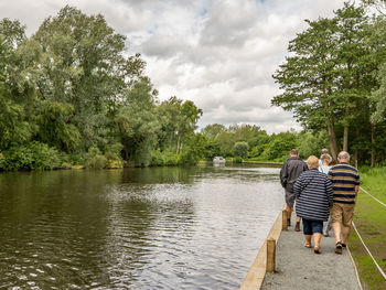 Rear view of couple walking by trees against sky