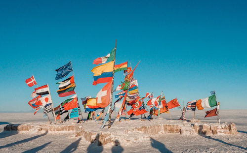 Multi colored flags on beach against clear blue sky