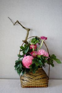 Close-up of pink flowers in basket on table against wall