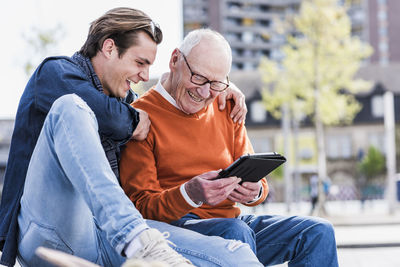 Happy senior man and adult grandson looking at tablet