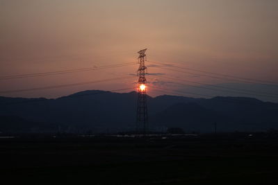 Silhouette electricity pylon by mountains against sky during sunset