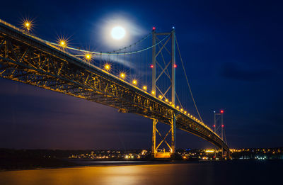 Low angle view of illuminated bridge over river against sky at night