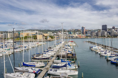 Sailboats moored in harbor by buildings against sky