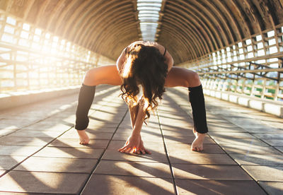 Full length of female athlete exercising on footbridge during sunset