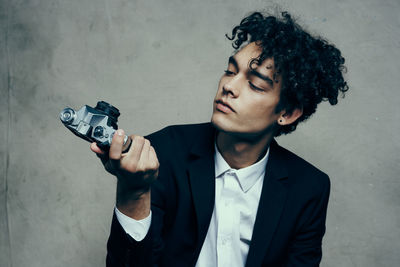 Portrait of young man holding camera while standing against wall