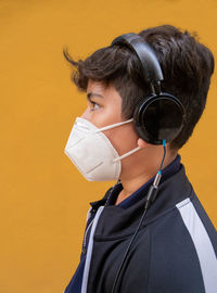 View of boy wearing mask and headphones against yellow wall.
