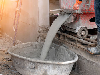 Low section of worker standing by equipment pouring cement in container at construction site