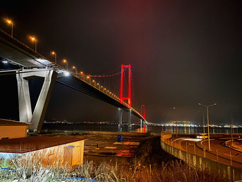 Illuminated bridge over river against sky at night