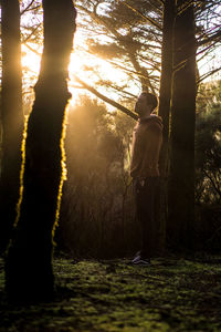 Side view of man standing by trees in forest