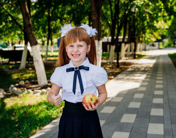 Back to school. a little schoolgirl stands in the school yard and holds an apple in her hands.