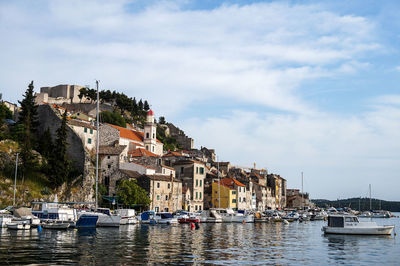 Sailboats moored in harbor against buildings in city