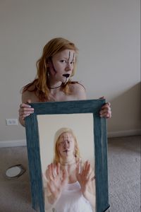 Portrait of young woman in halloween make-up holding picture frame at home