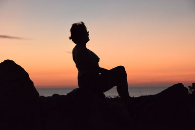 Silhouette woman sitting on rock against sky during sunset