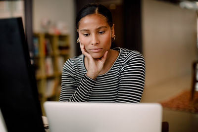 Serious female entrepreneur looking at laptop while sitting in workplace