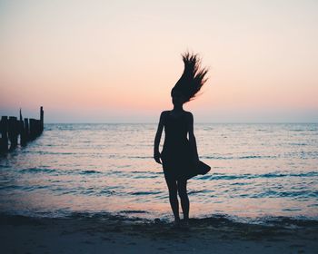 Silhouette woman standing at beach during sunset