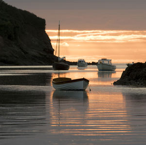 Sailboats moored on sea against sky during sunset