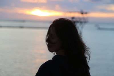 Side view of young woman looking at sea against sky during sunset