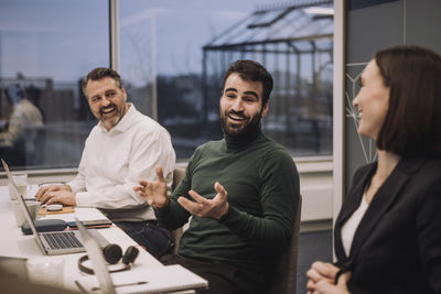 Happy businessman discussing with female and male colleagues in meeting at work place