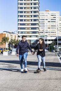 Happy couple skateboarding while holding hands on street