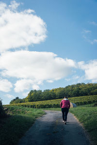 Rear view of woman walking on country road. rear view of woman walking on field against sky 