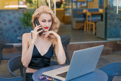 Beautiful woman in glasses sits at table in a street cafe and works on tablet