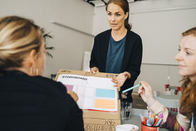 Confident female technicians explaining strategy on placard to manager at creative office