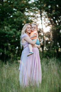 Happy pregnant woman carrying son while standing on field