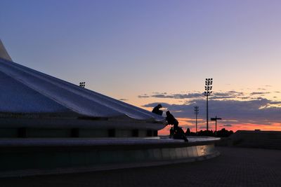 Side view of woman on roof against sky during sunset