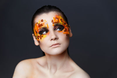 Close-up of shirtless young woman with eye make-up and rhinestones against gray background