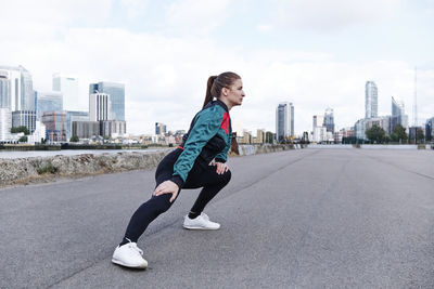 Sportswoman doing warm up exercise on promenade in city