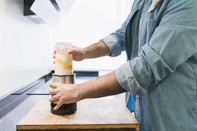 Man cooking in the kitchen in a denim shirt. an anonymous is going to beat a mixture of flour, eggs and milk