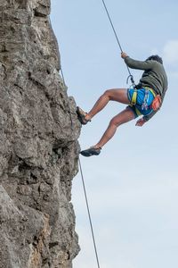 Low angle view of man climbing on rock against sky