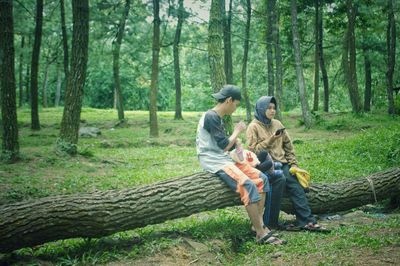 Full length of young couple sitting on fallen tree at forest