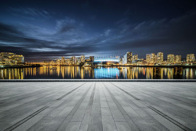 Illuminated buildings by sea against sky at night