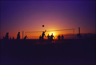 Silhouette people playing volleyball against clear sky during sunset