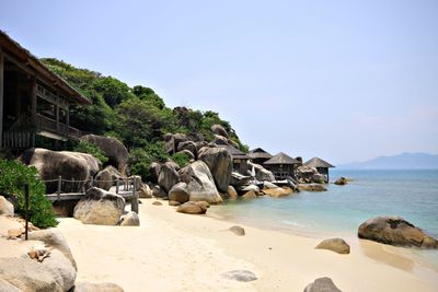 Stilt houses and mountain by beach against clear sky