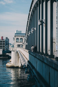 Bridge over river by buildings in city against sky