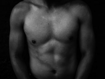 Midsection of shirtless man against black background