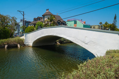 Arch bridge over river by buildings against sky