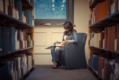 Young woman studying while sitting on armchair in library
