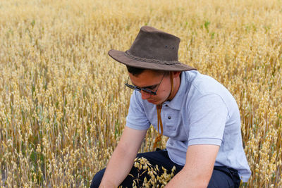 Harvester. portrait of farmer seating in gold wheat field with blue sky in background. young man