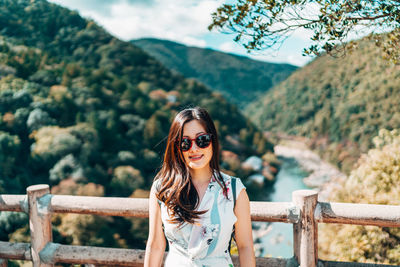 Portrait of smiling young woman in sunglasses against mountains