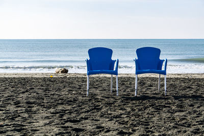 Chairs on beach against sea against sky