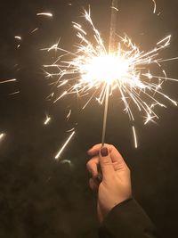 Cropped hand of woman holding sparkler at night