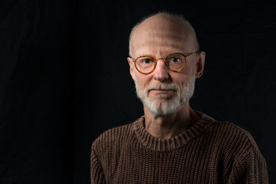 Portrait of smiling senior man wearing sweater against black background