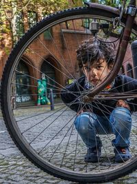 Portrait of boy crouching by bicycle wheel on footpath