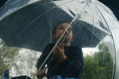 Low angle view of boy holding umbrella during monsoon