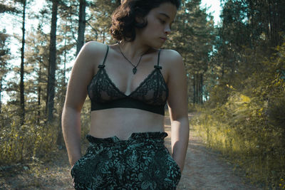 Close-up of young woman with hands in pockets standing in forest