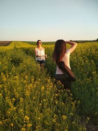 Friends standing amidst flowering plants on field against sky