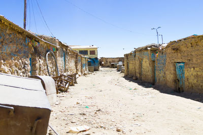 Street amidst abandoned buildings against clear blue sky